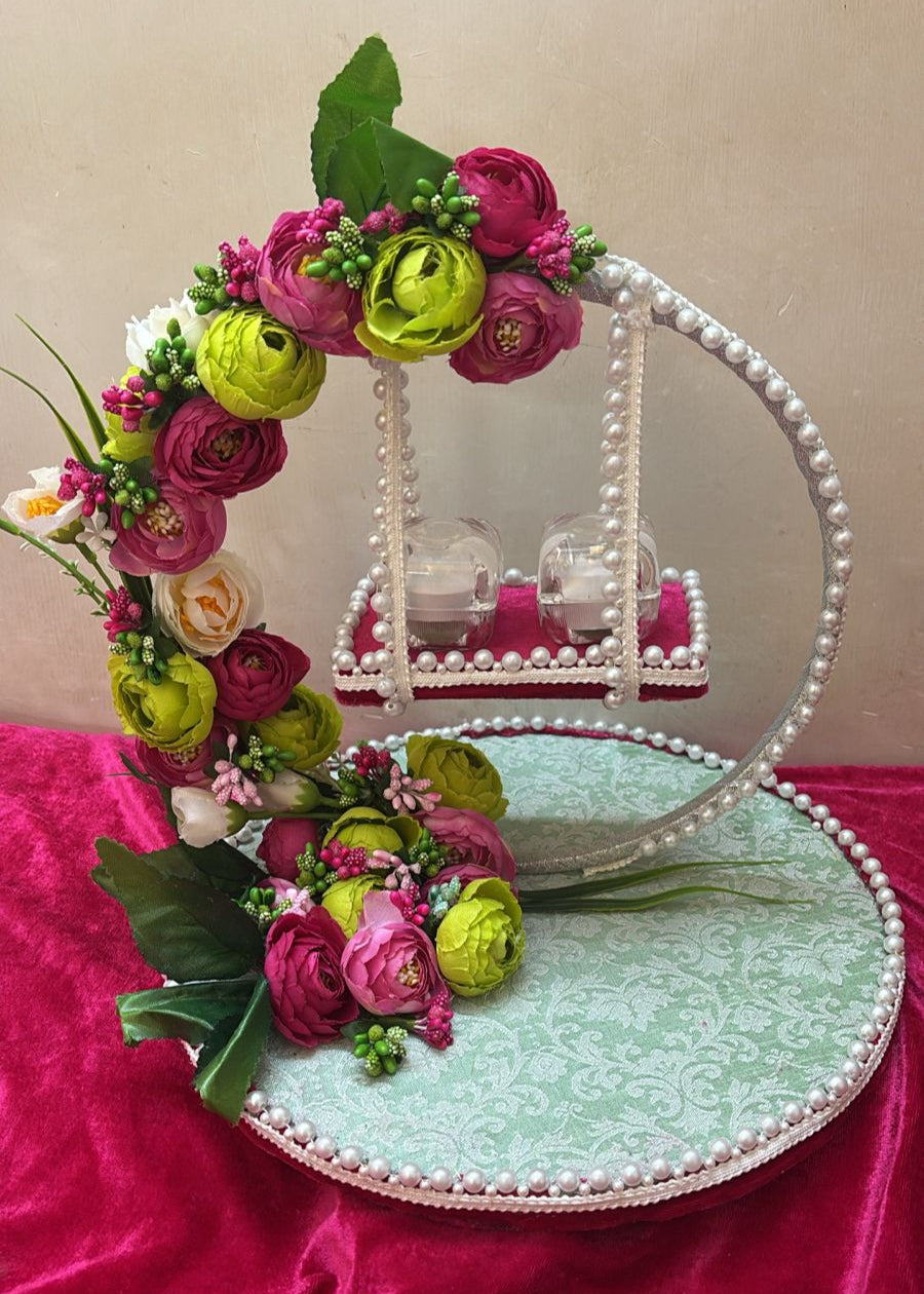 A decorative ring platter with a green base and white circular design, adorned with artificial flowers and pearls, displayed on a red fabric surface.