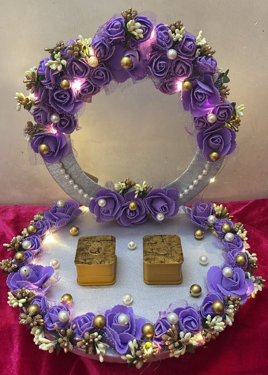 A handmade ring platter featuring a circular design with purple roses, pearls, and LED lights, accompanied by two small ring boxes on the base.