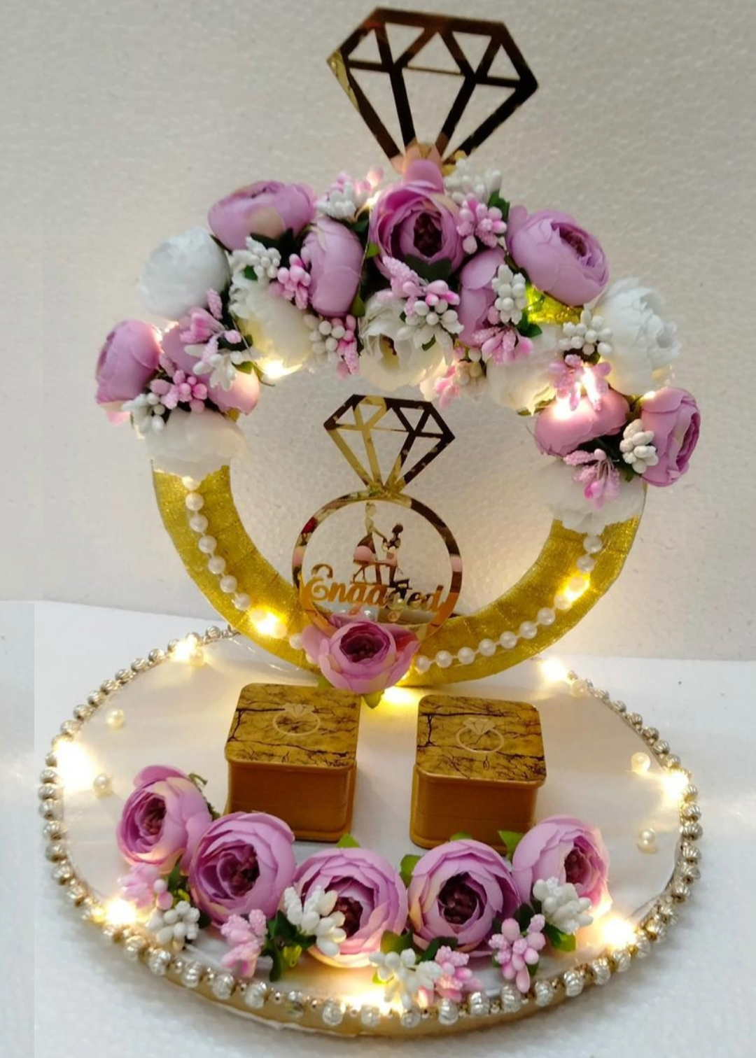 A decorative ring platter with a golden ring motif, surrounded by pink roses and small lights, displayed on a table at an event.