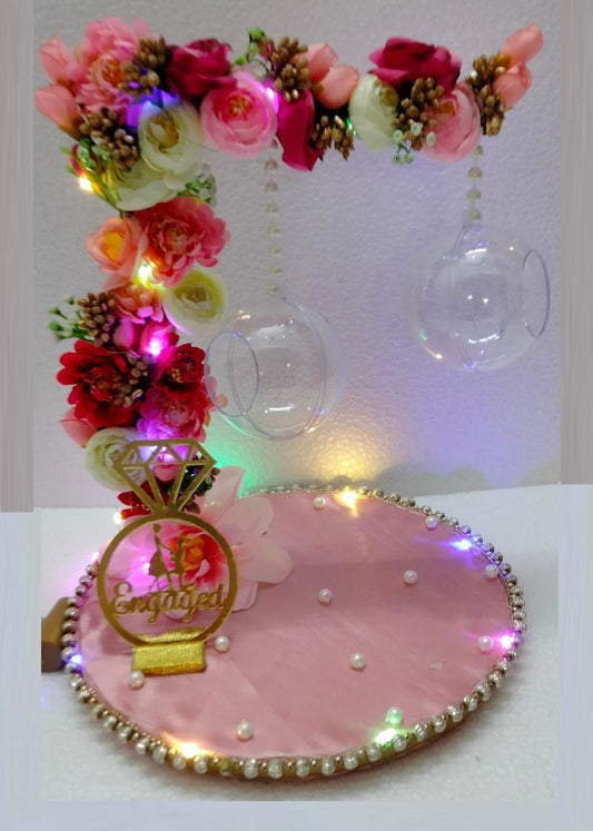 A decorative pink ring platter with a colorful floral arrangement, pearls, and LED lights, designed for ring ceremony purposes.