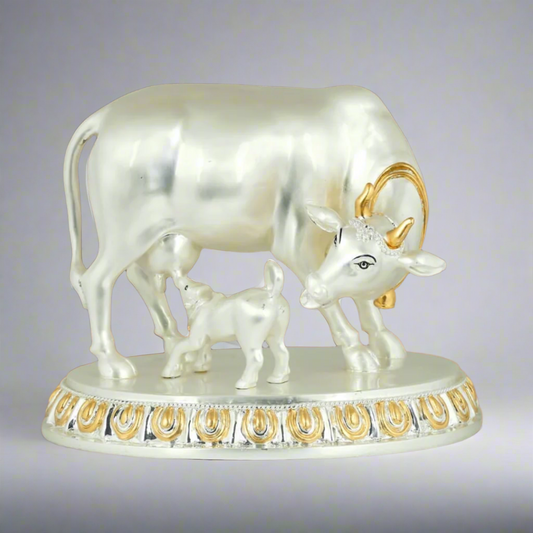 A 999 Pure Silver Plated statue of a Kamdhenu cow with a calf, placed on a decorative base with gold accents.
