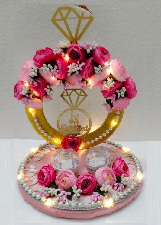 A decorative ring platter with a golden ring motif, surrounded by pink flowers and lit by fairy lights, displayed on a white background.