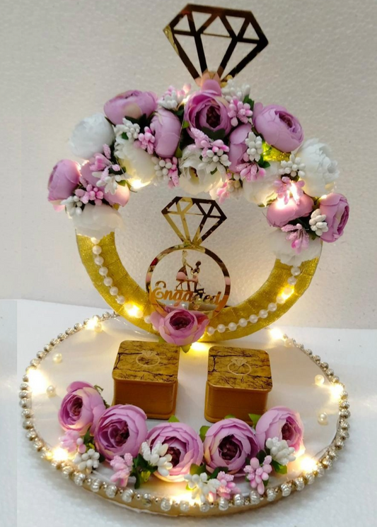 A decorative ring platter with a golden ring motif, surrounded by pink roses and small lights, displayed on a table at an event.