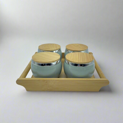 Set of four ceramic jars with wooden lids on a wooden tray against a white background
