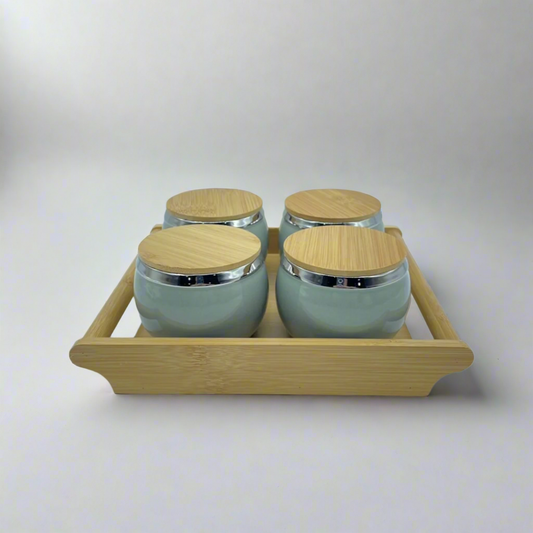 Set of four ceramic jars with wooden lids on a wooden tray against a white background